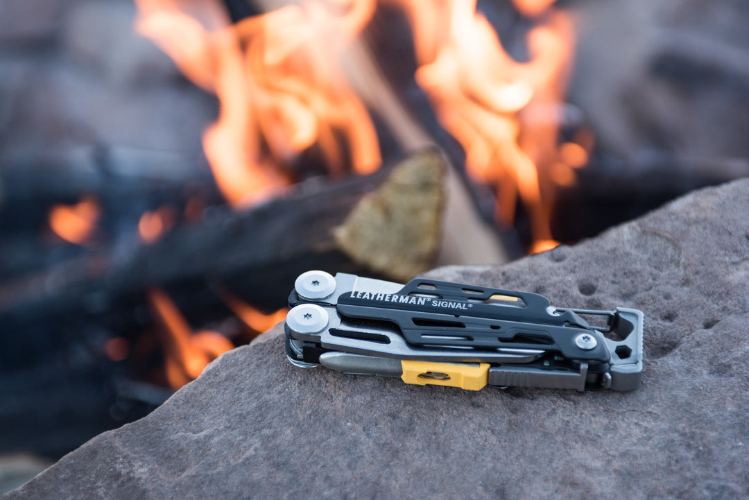 Leatherman Signal multi-tool resting on a rock beside a campfire