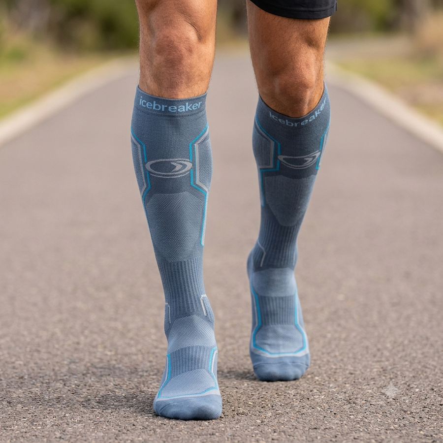 A close-up of a person's legs walking on a paved road, wearing matching blue compression sleeves with the brand name 'Icebreaker' visible near the top of each sleeve.