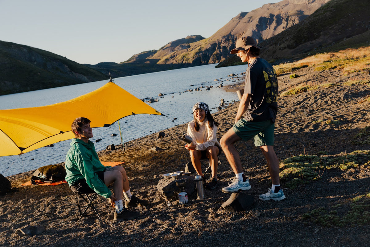 Hikers resting beside a yellow tarp at a mountain lake in Kolon Sport gear
