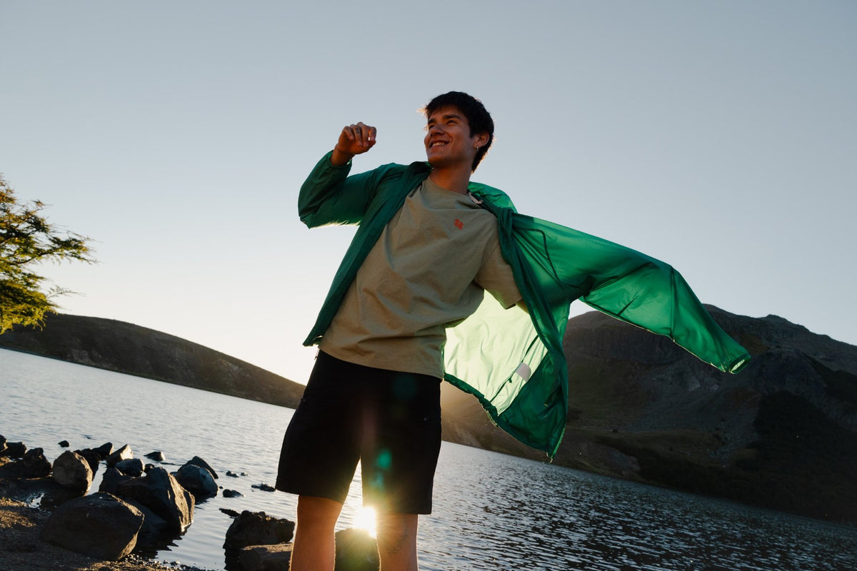 Hiker pulling on a green Kolon Sport jacket beside a lake
