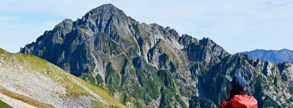 Hiker with a red Montbell backpack looking at a rocky mountain peak