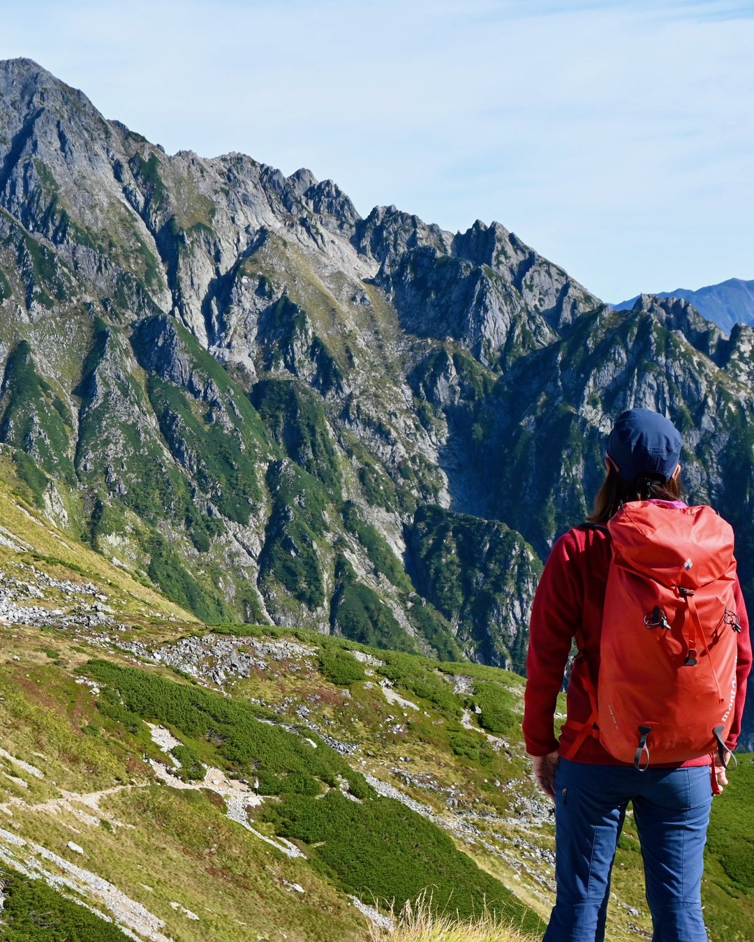Hiker with a red Montbell backpack looking at a rocky mountain peak